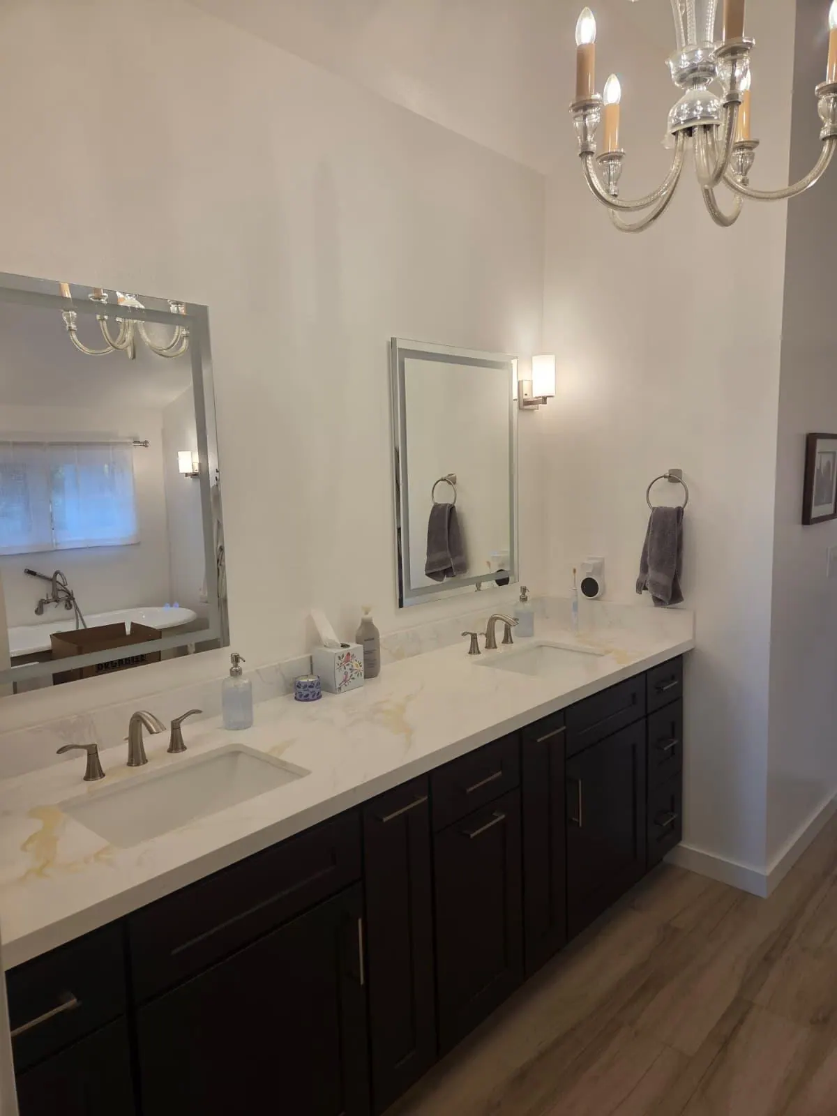New double vanity with dark cabinets, a white veined countertop, framed mirrors and wall sconces